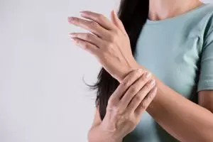 A mulher segura a lesão na mão do pulso, sentindo dor.